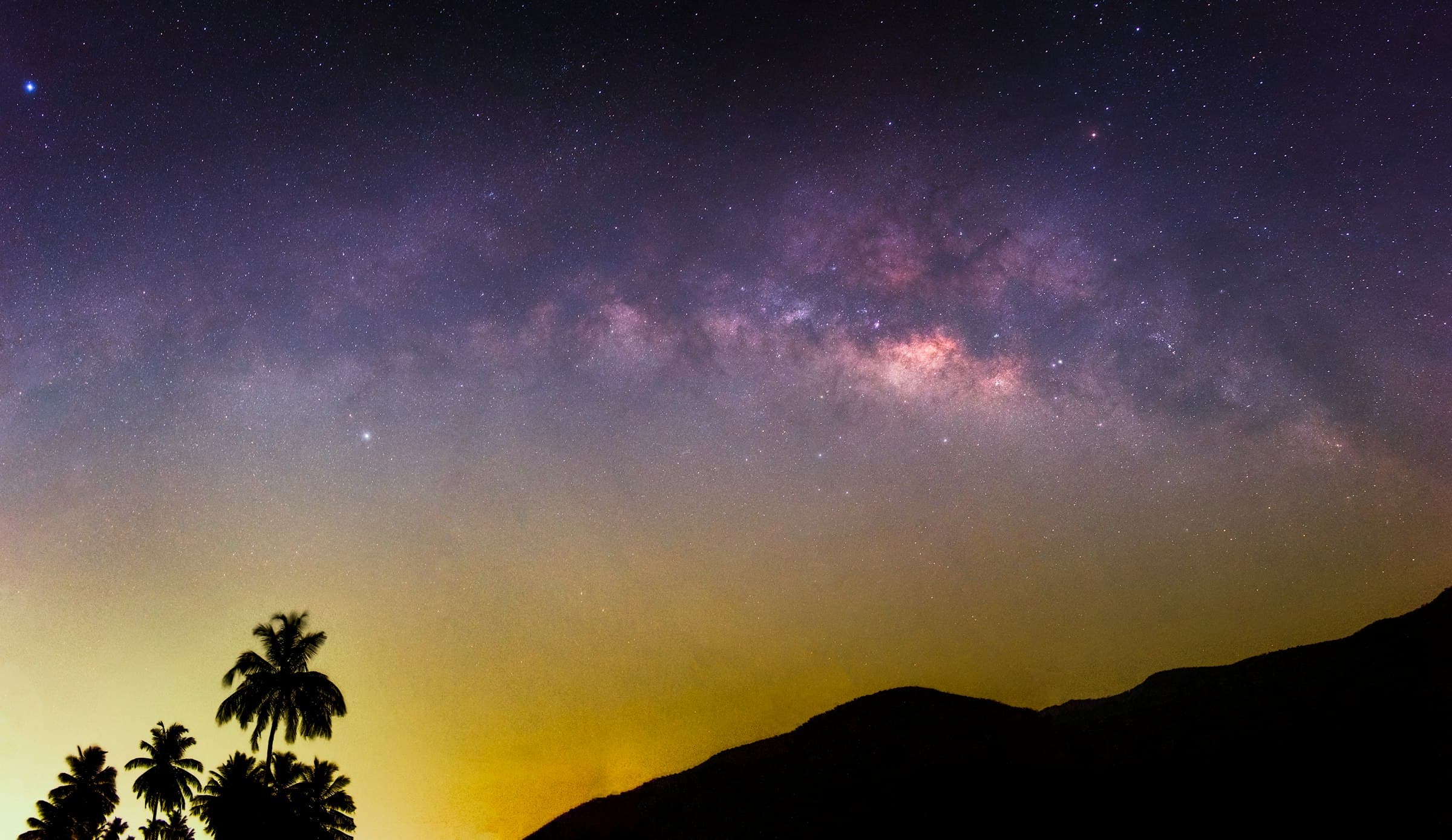 The Milky Way over palm trees and hills